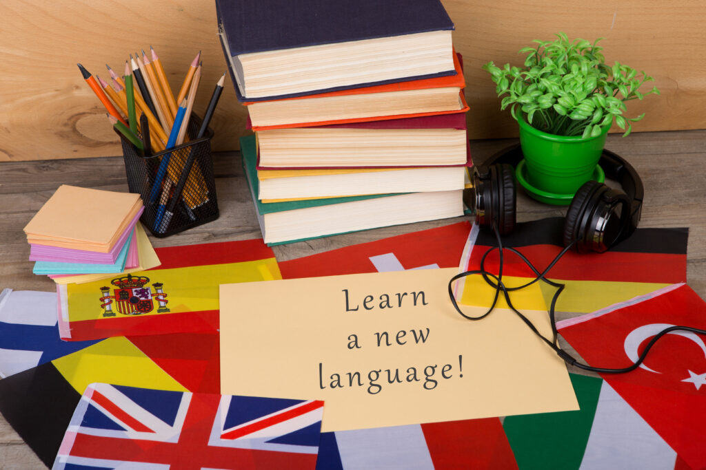 paper with text "Learn a new language!", flags, books, headphones, pencils